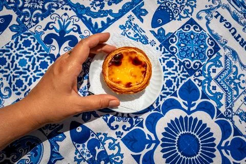 Hand serving one pastel de nata custard tart on blue tablecloth Stock Photos