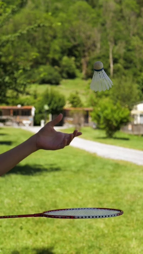 Hand serving a shuttlecock with a badminton racket on a sunny lawn Stock Footage 342520144