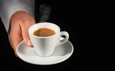 Hand serving steaming espresso cup on black background Stock Photos