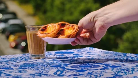 Hand serving three pastel de nata tarts beside meia de leite coffee Stock Footage 337723609