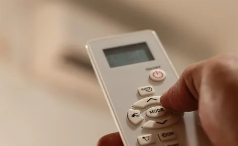 Hand sets the air conditioner temperature with a remote control in a bedroom Stockfoto's