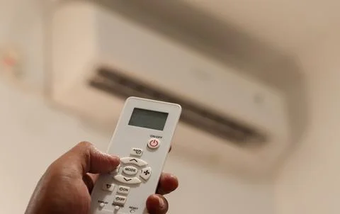 Hand sets the air conditioner temperature with a remote control in a bedroom Stockfoto's