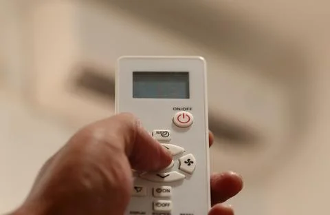 Hand sets the air conditioner temperature with a remote control in a bedroom Stockfoto's