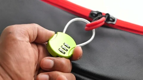 A hand is setting the combination lock attached to the zipper of a bag 스톡 동영상 348259862