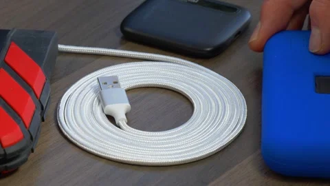 A hand setting down portable hard drives, next to a coiled USB-A cable or cord. Video stock 292010965