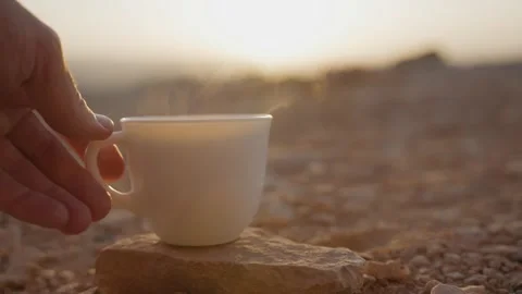 Hand setting hot drink cup with steaming tea or coffee on desert rock or stone Stock Footage 316068939