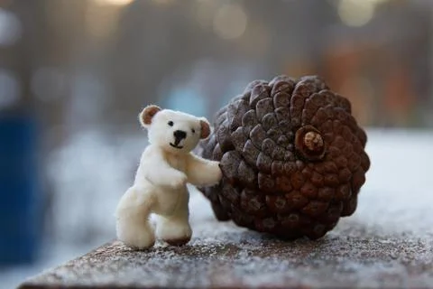 Hand-sewn micro-plush teddy bear rolls a large fir cone. Stock Photos