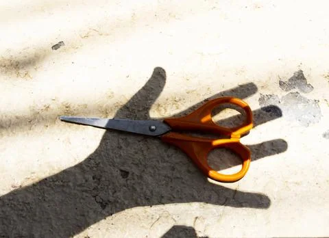 Hand shadow over a pair of orange scissors Fotos Stock