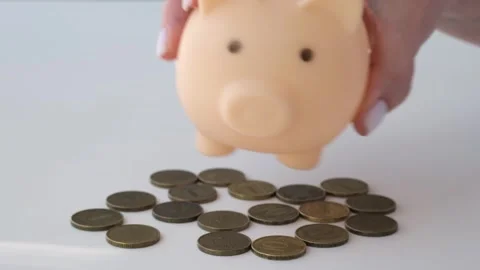 Hand shaking empty piggy bank above white table and lay it on coins upside down Stock-Footage 295787873