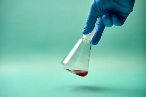 Hand shaking an Erlenmeyer flask with a red chemical. Stock Photos