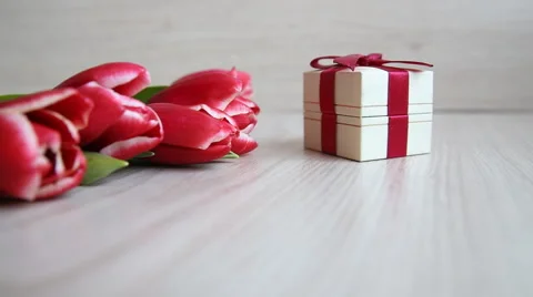 Hand shifts gift box with a red bow next to the tulips Stock Footage 60048445