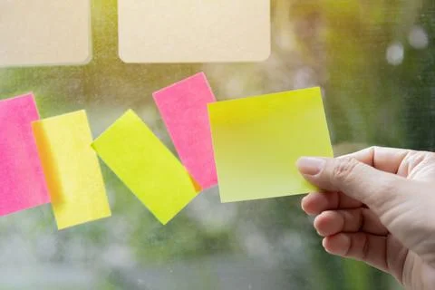 A hand shoots multi-Colored square post-it notes pasted on a glass  wall. Stock Photos