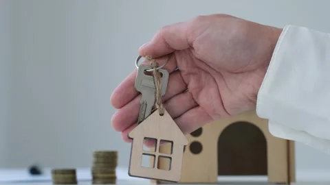 Hand showing house key on background of house model and coins. Buying own home Stock Footage 269545574