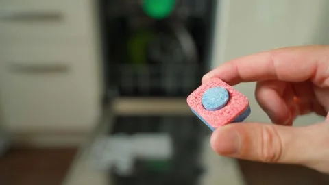 A hand shows a dishwasher tablet close-up against the background of an open Stock Footage 253171088