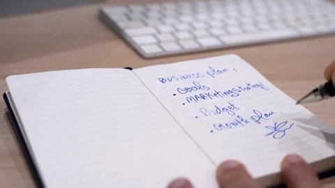 Hand Signing Business Plan in Notebook on Office Desk with Keyboard Background Stock Footage 332073336