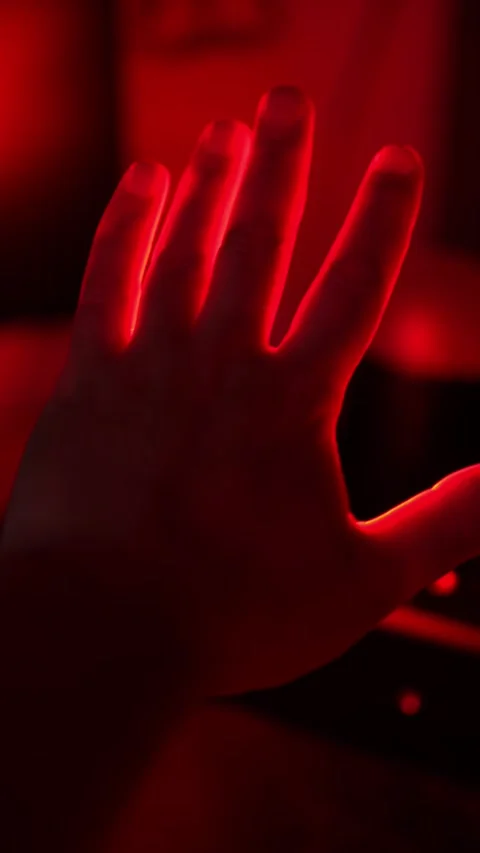 Hand silhouette with bright red glowing light between fingers, dark Stock Footage 332600565