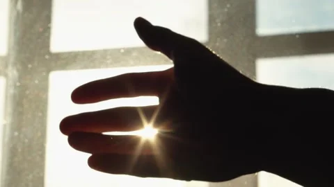 A hand silhouette on a window lets sunlight filter through, creating a serene 스톡 동영상 283202459