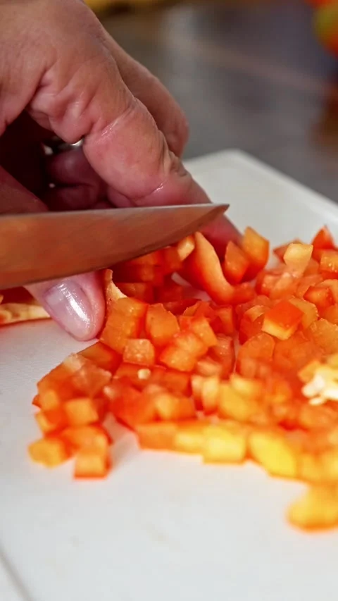 A hand skillfully chopping vibrant orange bell peppers on a rustic cutting board Stock Footage 314893974