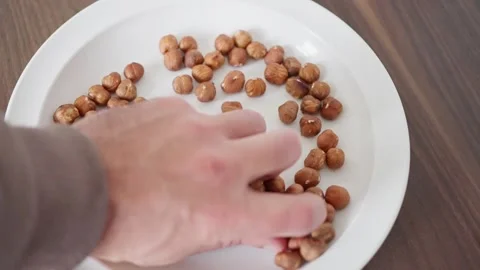 A hand skillfully grabbing some delicious hazelnuts from an appealing plate full Stock Footage 308663891