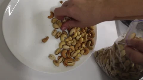 A hand is skillfully sorting through a variety of nuts on a plate, selecting the Stock Footage 292753014