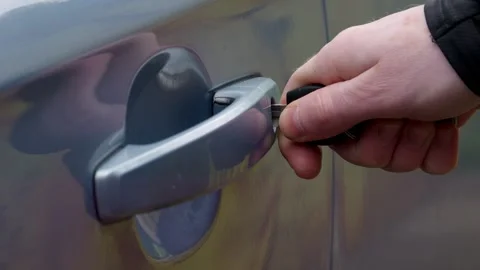 A hand skillfully using a key to unlock a car door, beautifully capturing the Stock Footage 309334163