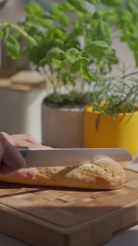 Hand slices bread on cutting board, with potted herbs in the background Stock Footage 340039986