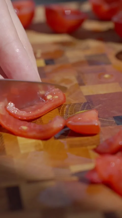 Hand slices a small tomato with knife on wooden cutting board Stock Footage 337198755