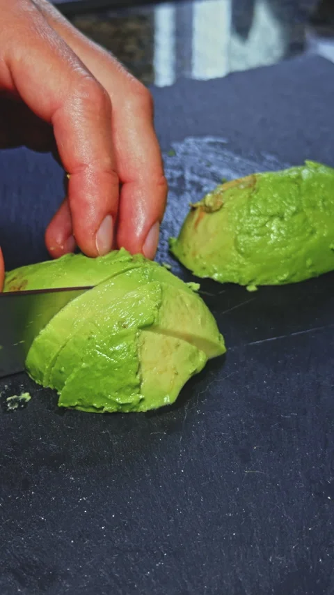 Hand slicing an avocado on a dark surface Stock Footage 277727026