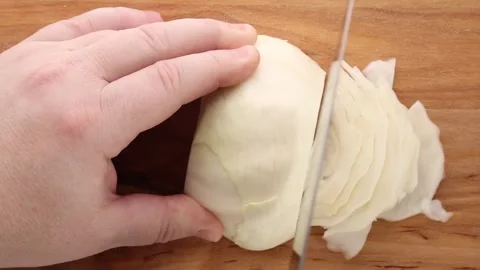 A hand slicing a cabbage into thin layers on a wooden surface. Stock Footage 311046501
