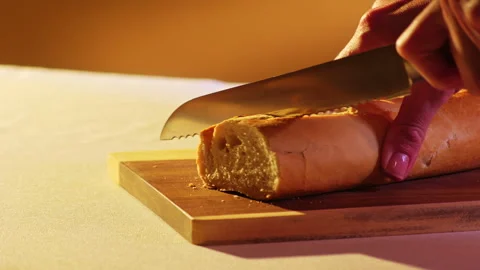 Hand Slicing Fresh Baguette with Bread Knife on Wooden Cutting Board Warm Light Stock Footage 334266346