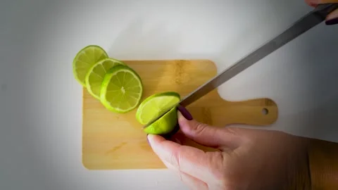 Hand Slicing Fresh Lime into Thin Pieces on Wooden Cutting Board Stock Footage 318246710