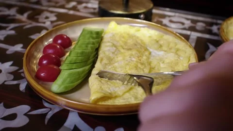 Hand Slicing Omelette with Cucumber and Cherry Tomatoes on Traditional Plate Stock Footage 345953701