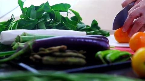 Hand slicing tomato on a kitchen table with vegetables Stock Footage 116013805