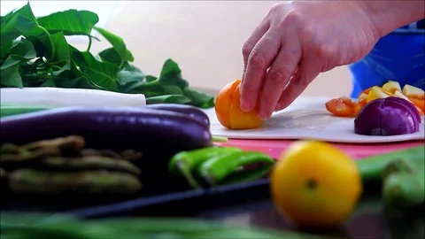 Hand slicing tomato on a kitchen table with vegetables Video stock 116014333