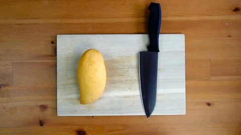 Hand slicing a yellow ripe mango on a chopping board. Stock Footage 129279568