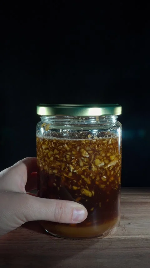 Hand sliding a jar of fermented ginger honey into frame on wooden table Stock Footage 324921715