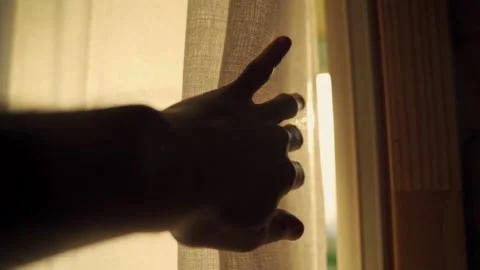 Hand slowly pulls away window curtain to reveal sunlight coming in the room Stock Footage 149437023