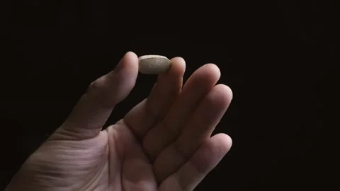 Hand slowly turning to show pill on dark background closeup Stock Footage 342240069