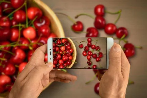 Hand with smarphone green spring red cherries on wooden background selective  Stock Photos