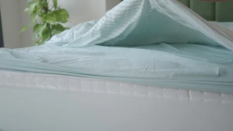 Hand smoothing blue bed sheet over white mattress and striped duvet. Stock Footage 332041414