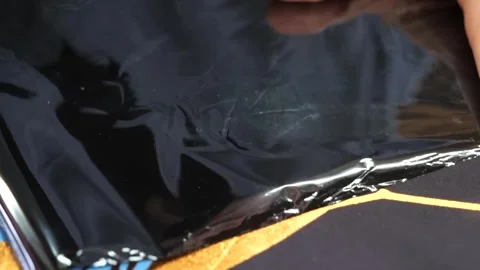Hand smooths a protective cellophane wrap over a glossy black lacquered fabric Stock Footage 339126263