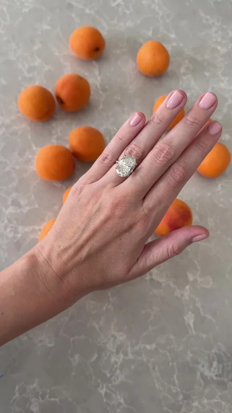 Hand with solitaire oval diamond engagement ring over apricots vertical video 스톡 동영상 317021972