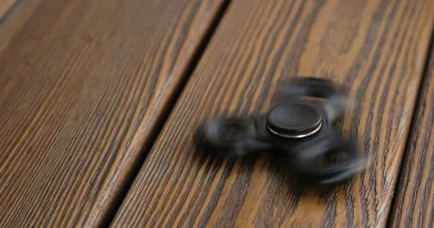 Hand spinner, or fidgeting spinner, rotating on the floor. wooden background. Vídeo Stock 76630133
