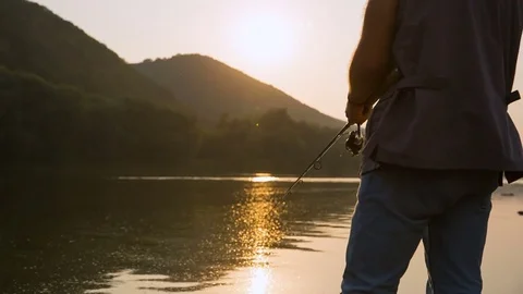 Hand with spinning and reel on the evening summer lake Stockbeeldmateriaal 80494765