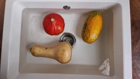 Hand spinning pumpkin in water in kitchen sink Video stock 330967967