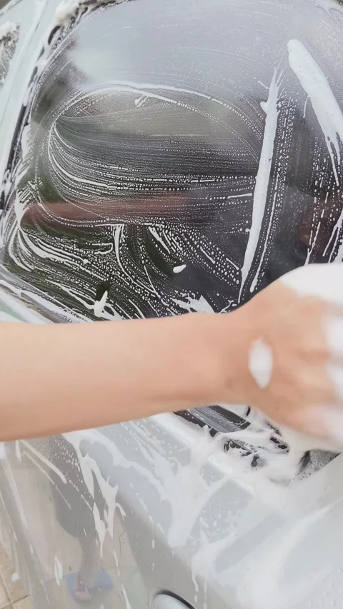 Hand with a sponge washing a soapy car window. Vehicle cleaning. Stock Footage 313299779