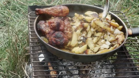 A hand with a spoon mixes potatoes with chicken drumsticks, fried in a fryin Vídeos de archivo 205872588