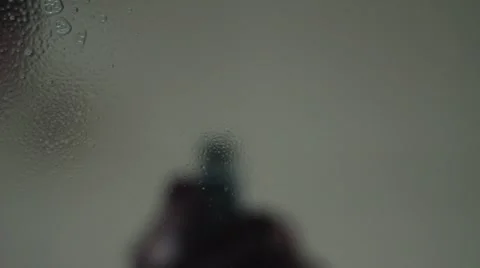 Hand spray liquid on glass to the camera. Drops flow down on glass Stock Footage 63161146