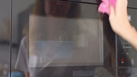 Hand sprays cleaner across microwave door and wipes wet surface with cloth Stock Footage 346729521