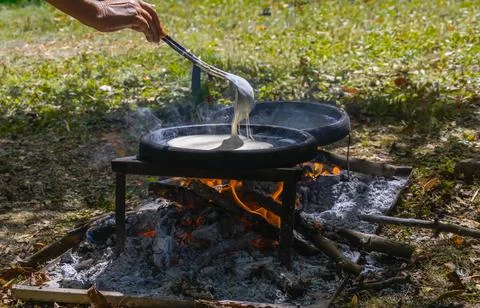 Hand spreading pancake batter on round griddles over wood fire during tradi.. Stock Photos